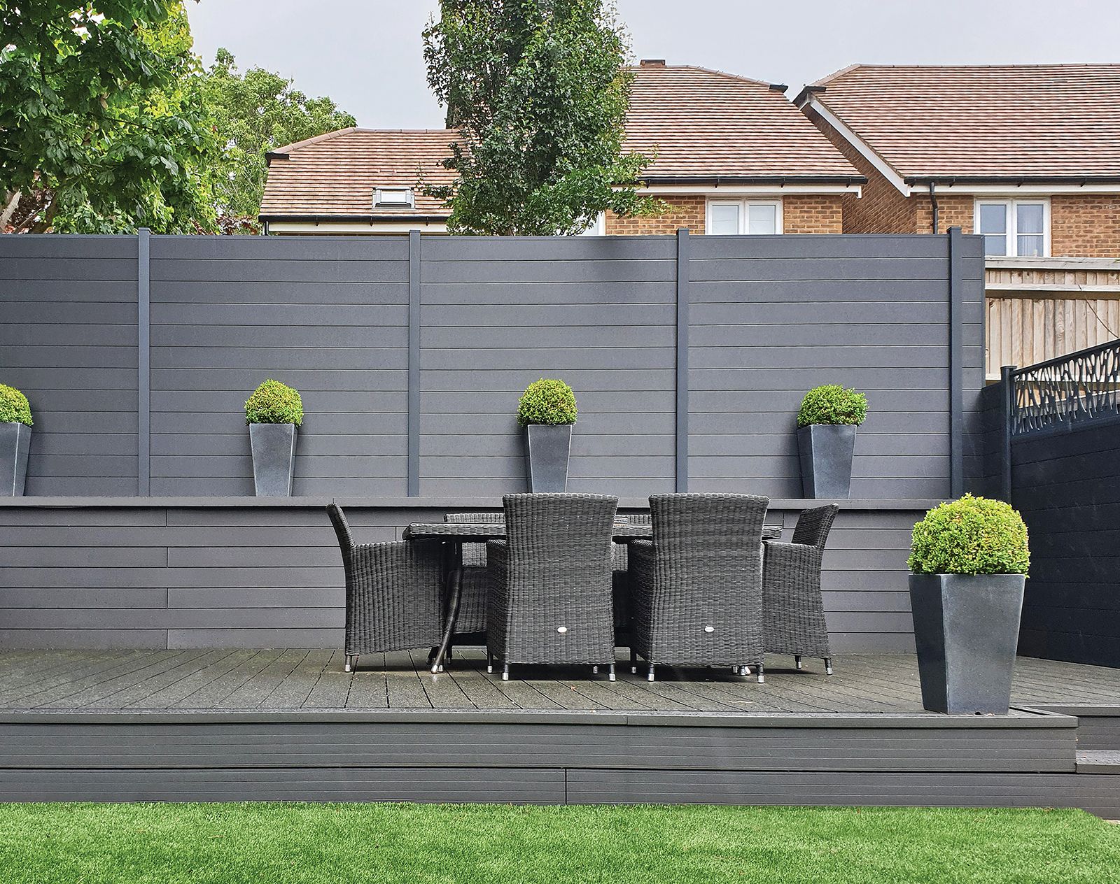 Grey composite fencing panels surrounding a raised decking area with rattan outdoor dining set and decorative planters, creating a private modern garden space.