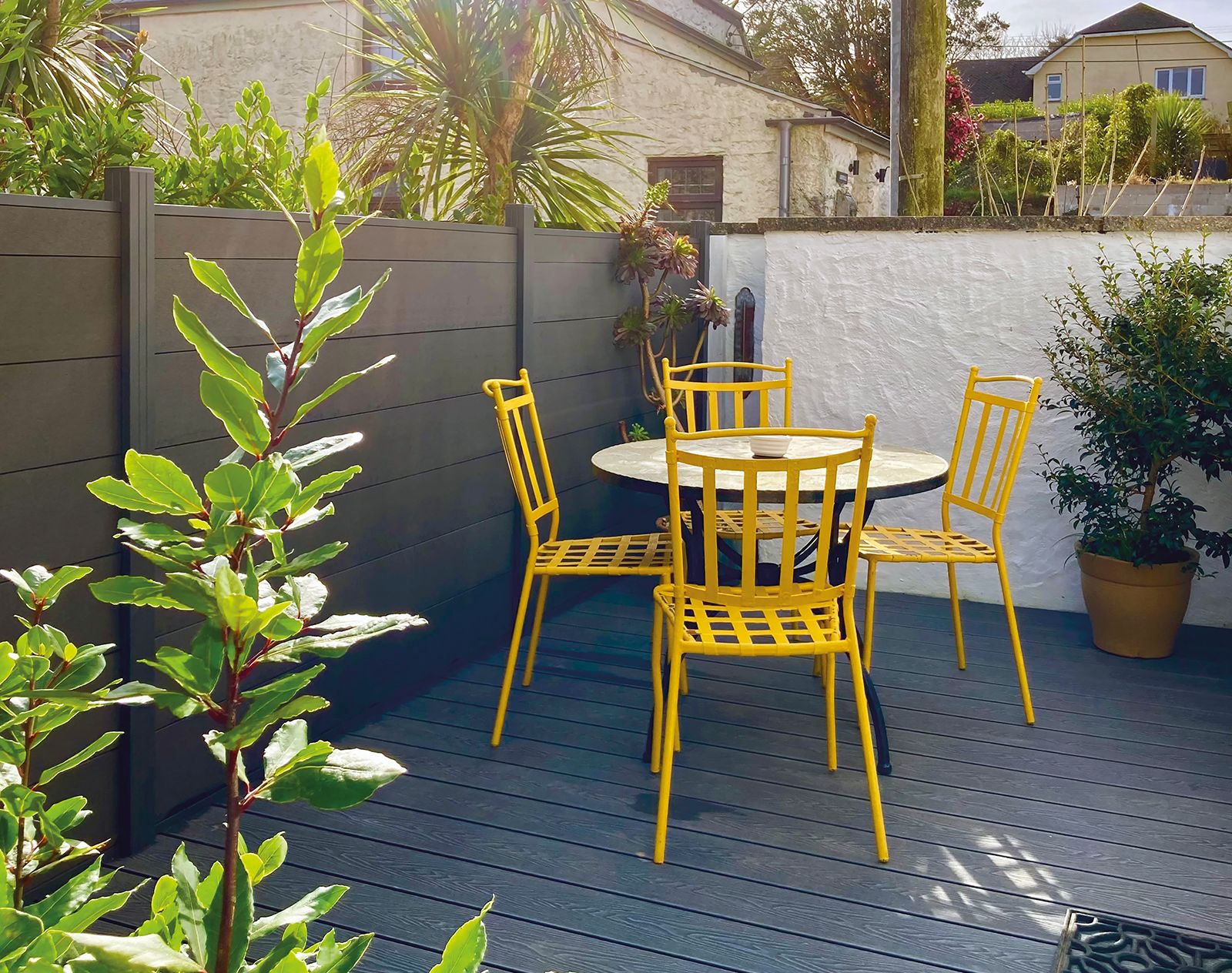 Dark grey composite fencing enclosing a small patio area with bright yellow metal chairs, potted plants, and grey decking, creating a colourful and private garden corner.