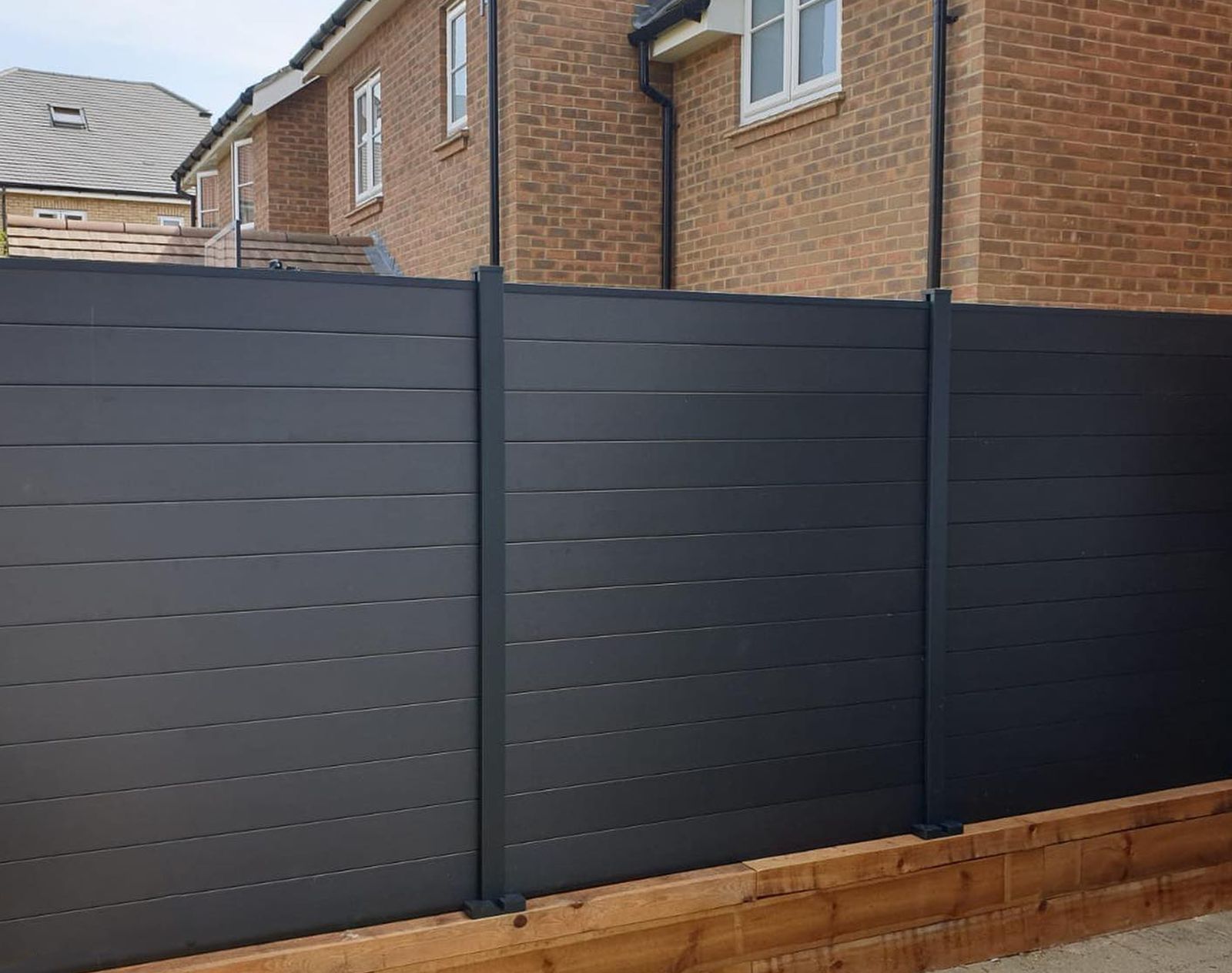 Dark grey composite fencing panels with clean horizontal lines, installed above a timber sleeper base in a modern suburban garden.
