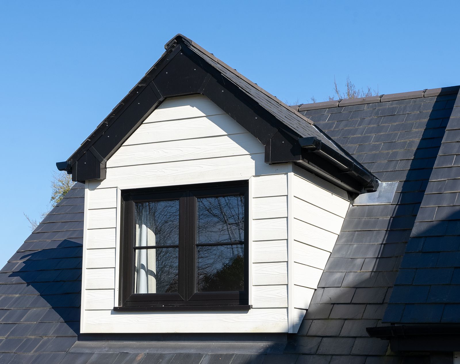 Dormer window finished with white fibre cement cladding in a horizontal layout, framed by a tiled roof and black window trim for a clean, modern contrast.