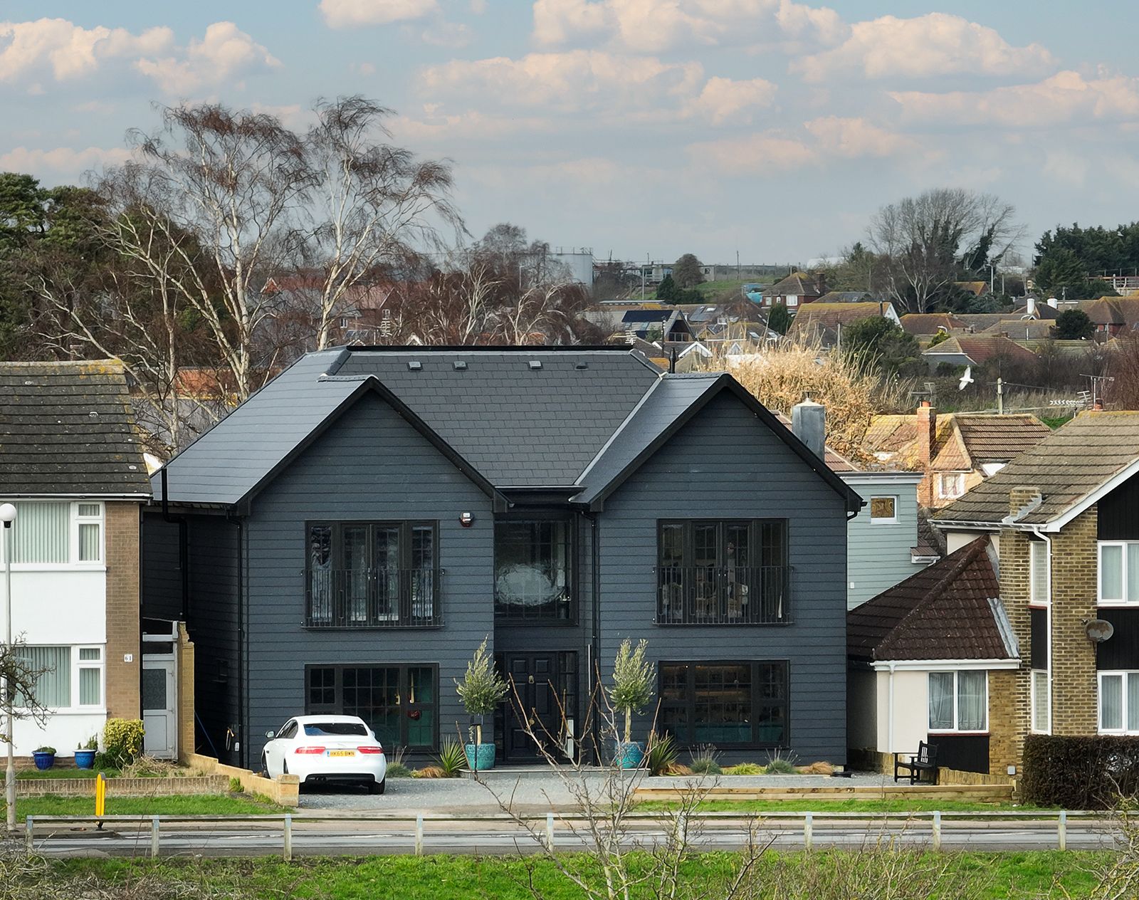 Contemporary two-storey home with dark grey fibre cement cladding and black-framed windows, creating a bold modern exterior in a residential street setting.