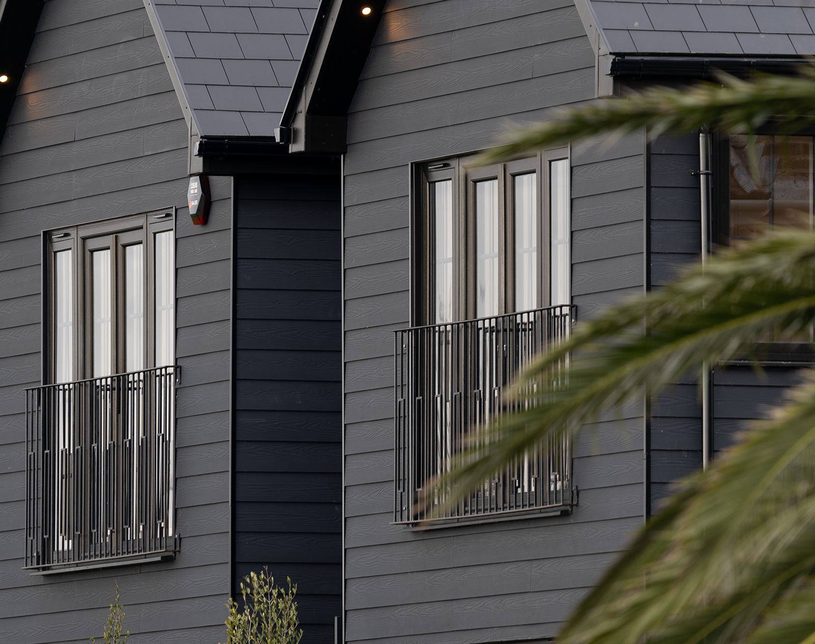 Contemporary house exterior featuring dark grey fibre cement cladding with Juliet balconies and slate roof tiles.