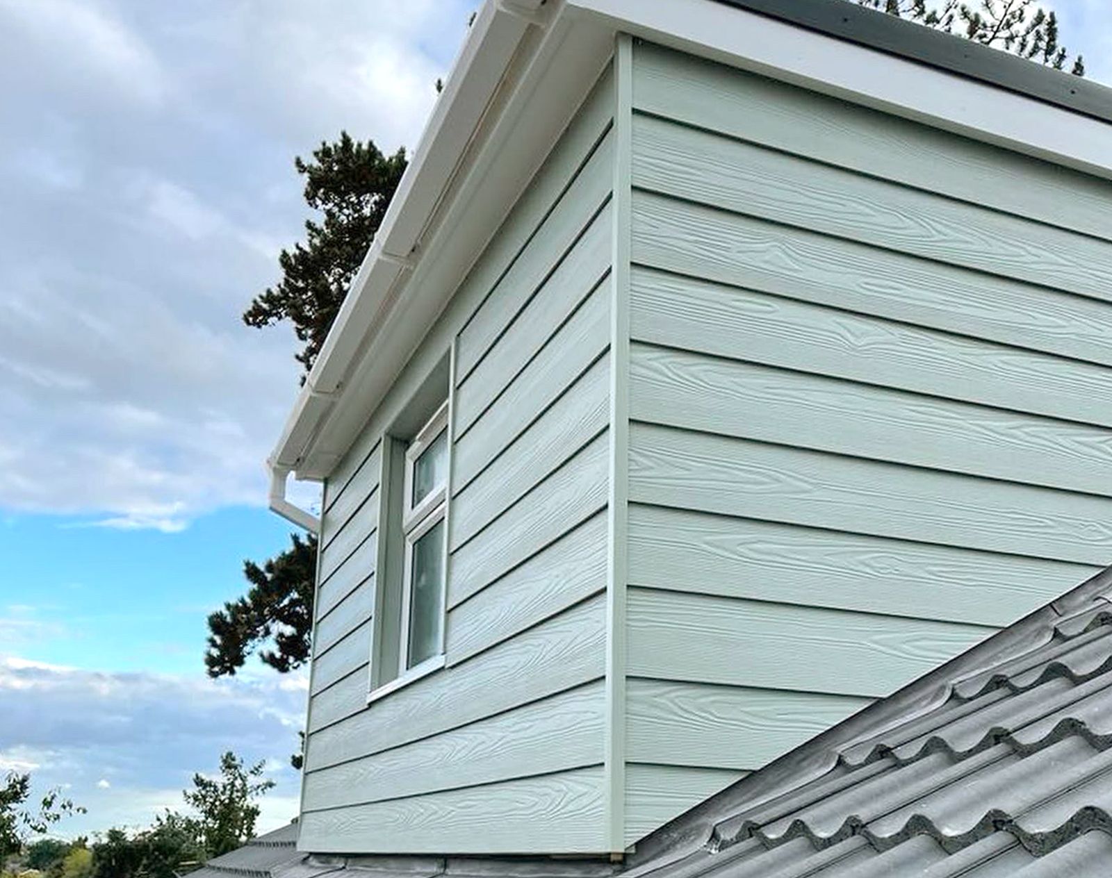 Light green fibre cement cladding installed on a dormer extension, with woodgrain texture and white uPVC window and trim detailing.