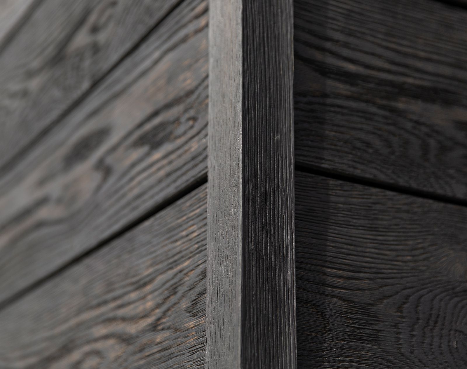 Close-up view of textured black Millboard cladding with realistic wood grain detail and seamless corner trim.