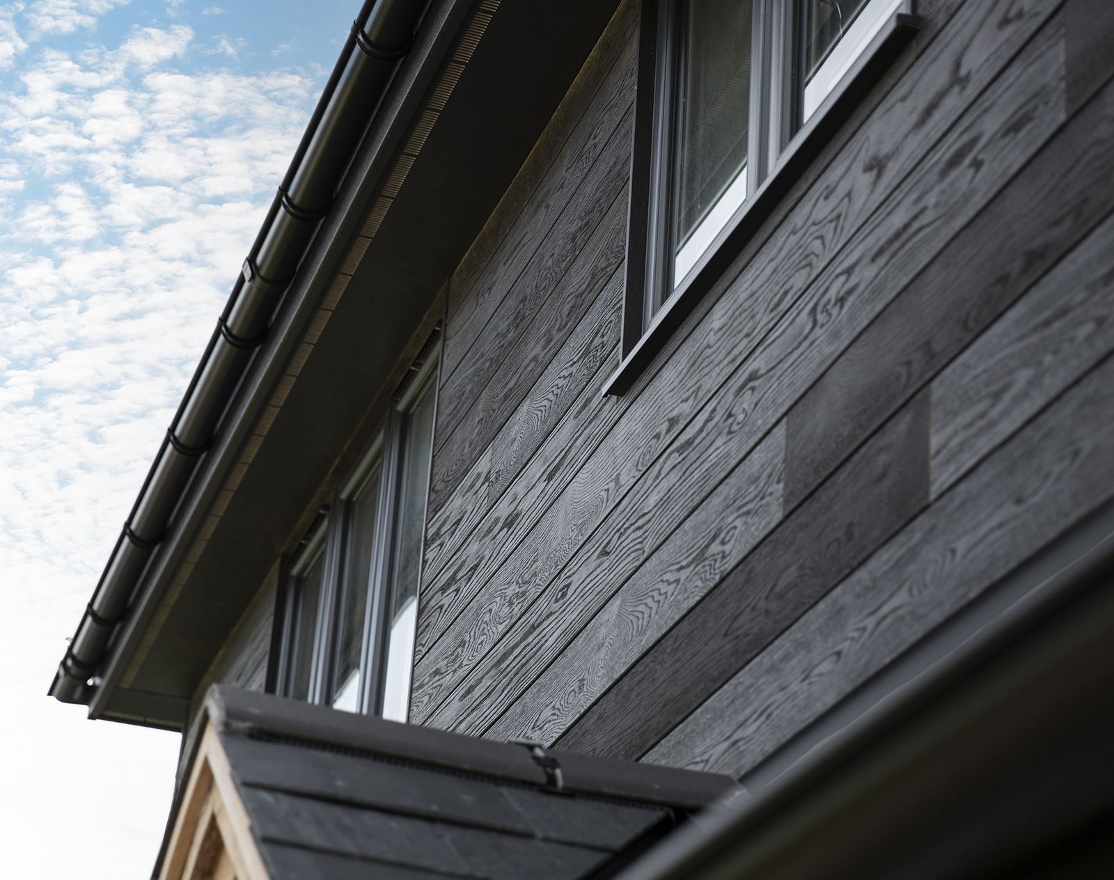 Close-up view of textured black Millboard cladding on a modern house exterior with double-glazed windows.
