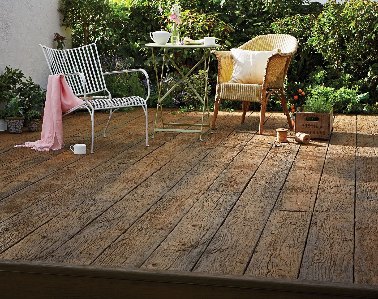 Rustic-style garden patio featuring Millboard decking in a weathered oak finish, with outdoor furniture and lush planting in the background.