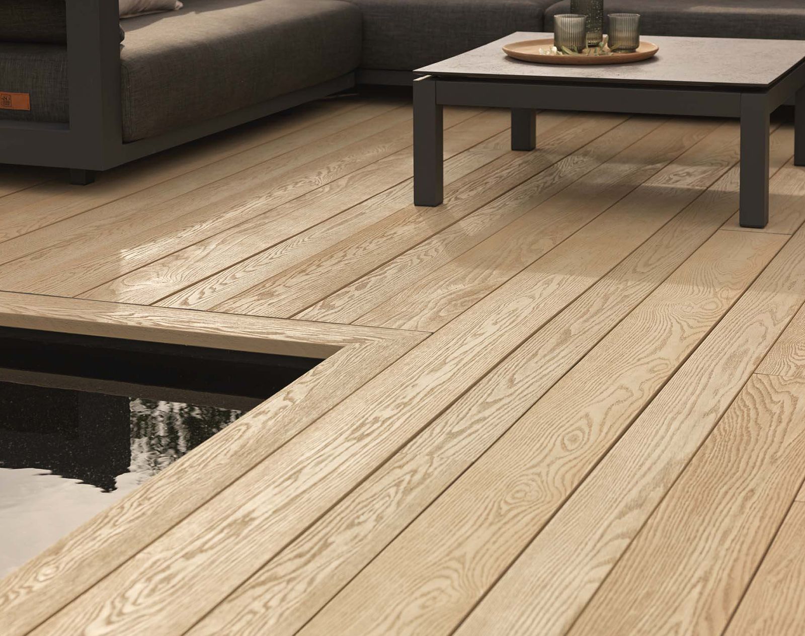 Light oak-effect Millboard decking surrounding a modern outdoor seating area with a water feature and minimalist coffee table.