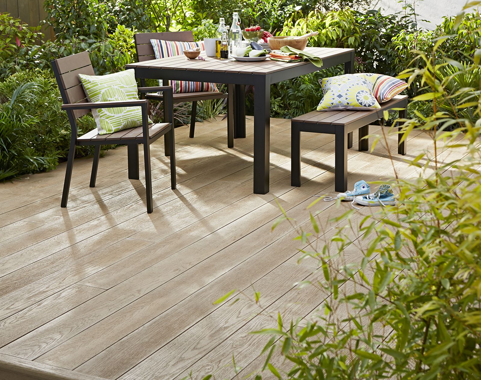 Millboard decking in a light wood finish with a modern garden dining set surrounded by lush greenery and playful outdoor accessories.