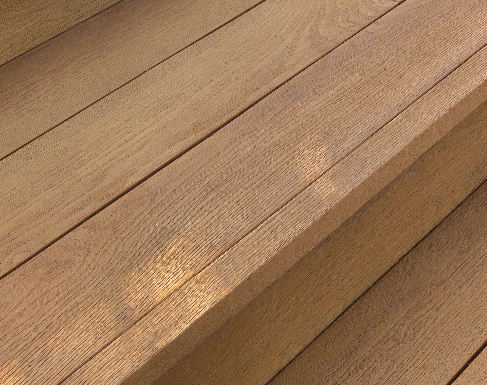 Golden-toned Millboard decking step detail showing realistic wood grain texture and precise edging.