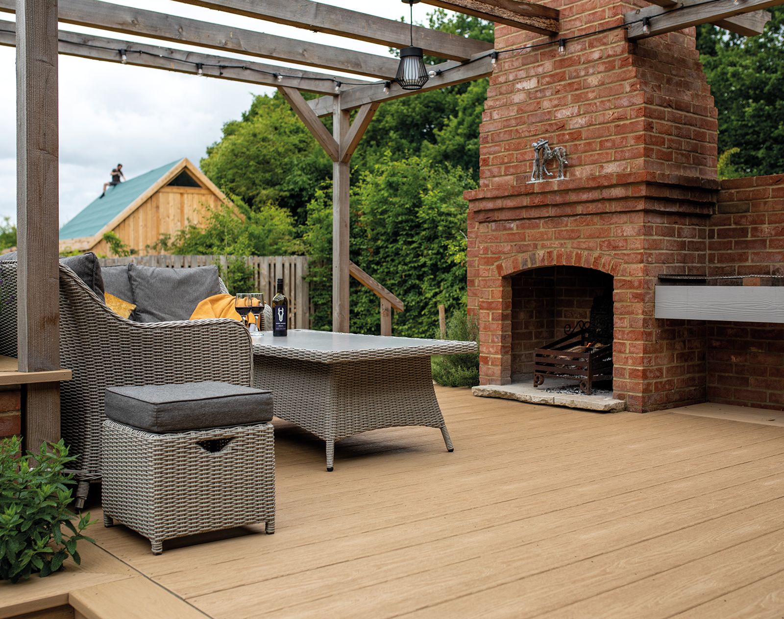 Outdoor seating area with wicker furniture and a brick fireplace set on natural wood-look Nordeck PVC decking, ideal for stylish and low-maintenance patios.
