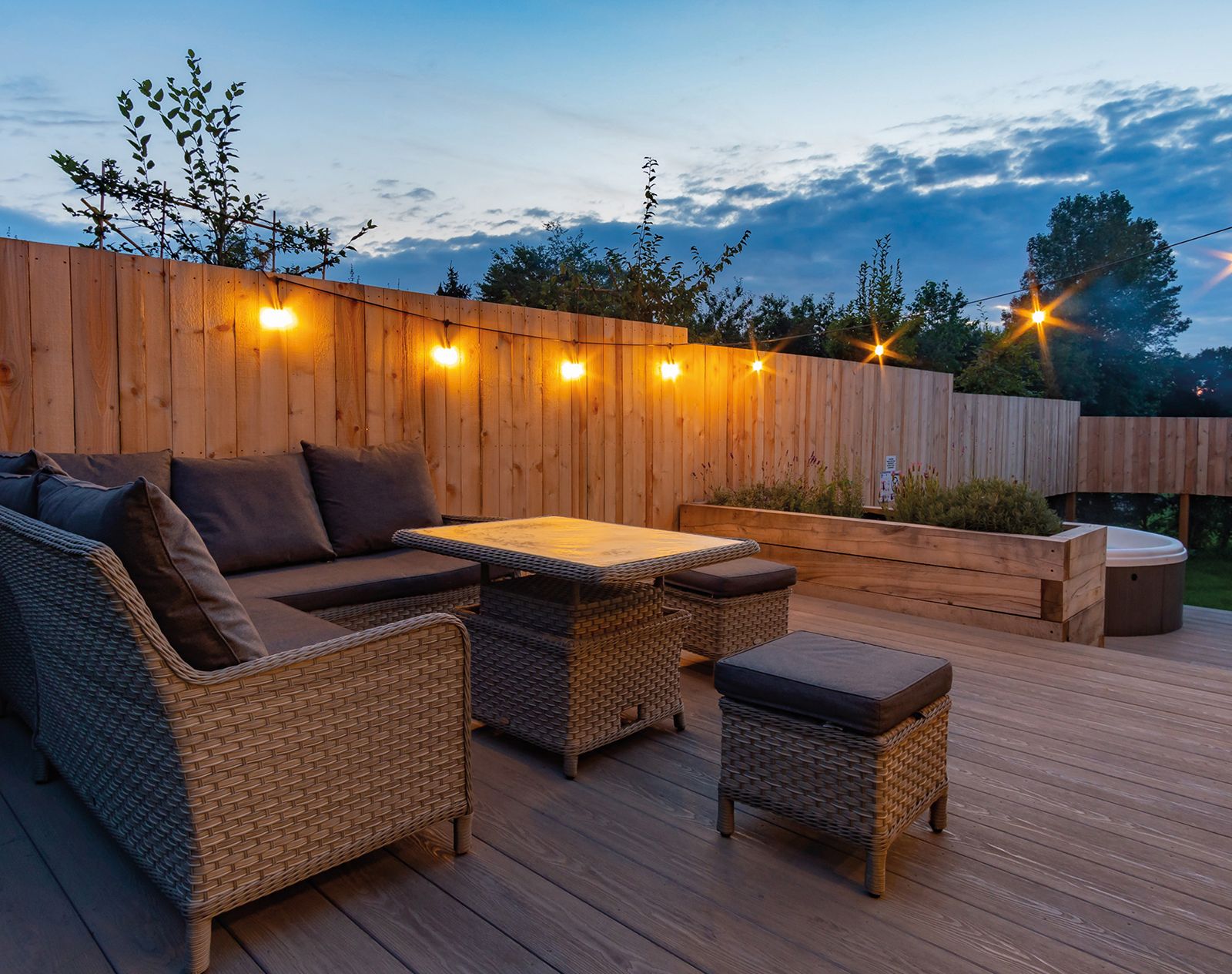 Outdoor seating area at dusk featuring Nordeck PVC decking in grey woodgrain finish, with string lights, rattan furniture, and timber fencing.