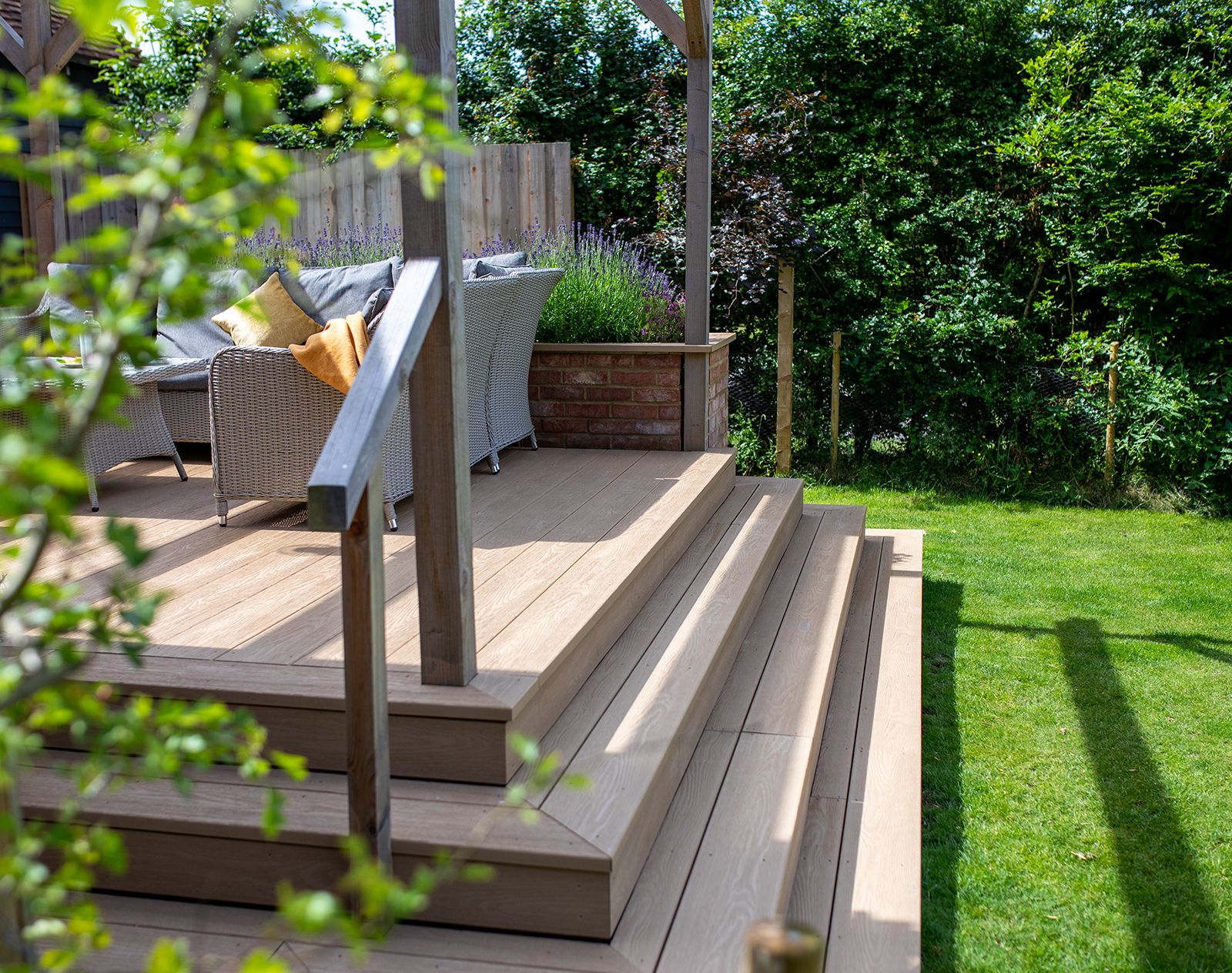 Raised garden patio with steps built using Nordeck PVC decking in natural wood tone, featuring rattan seating and lush greenery.