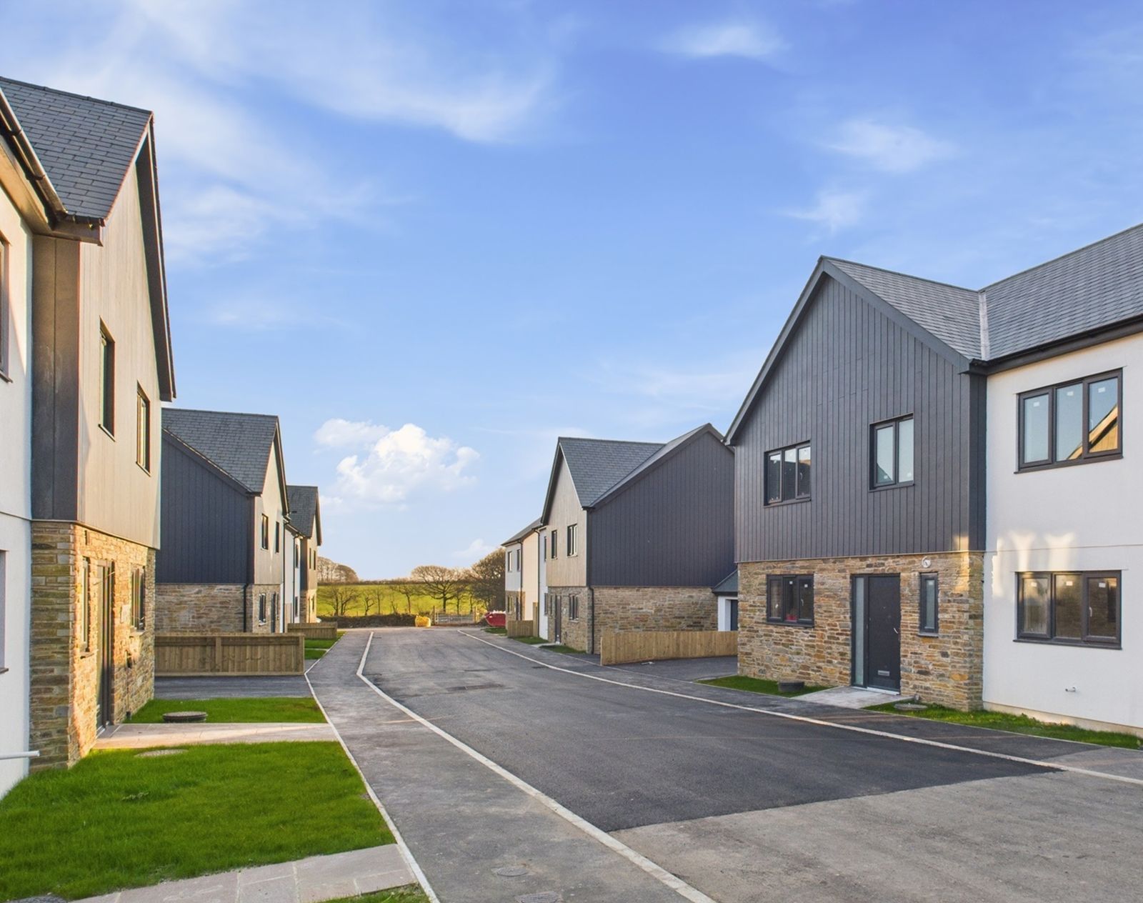New-build housing development featuring dark grey vertical composite cladding on upper storeys, paired with stonework and render for a modern, low-maintenance exterior.