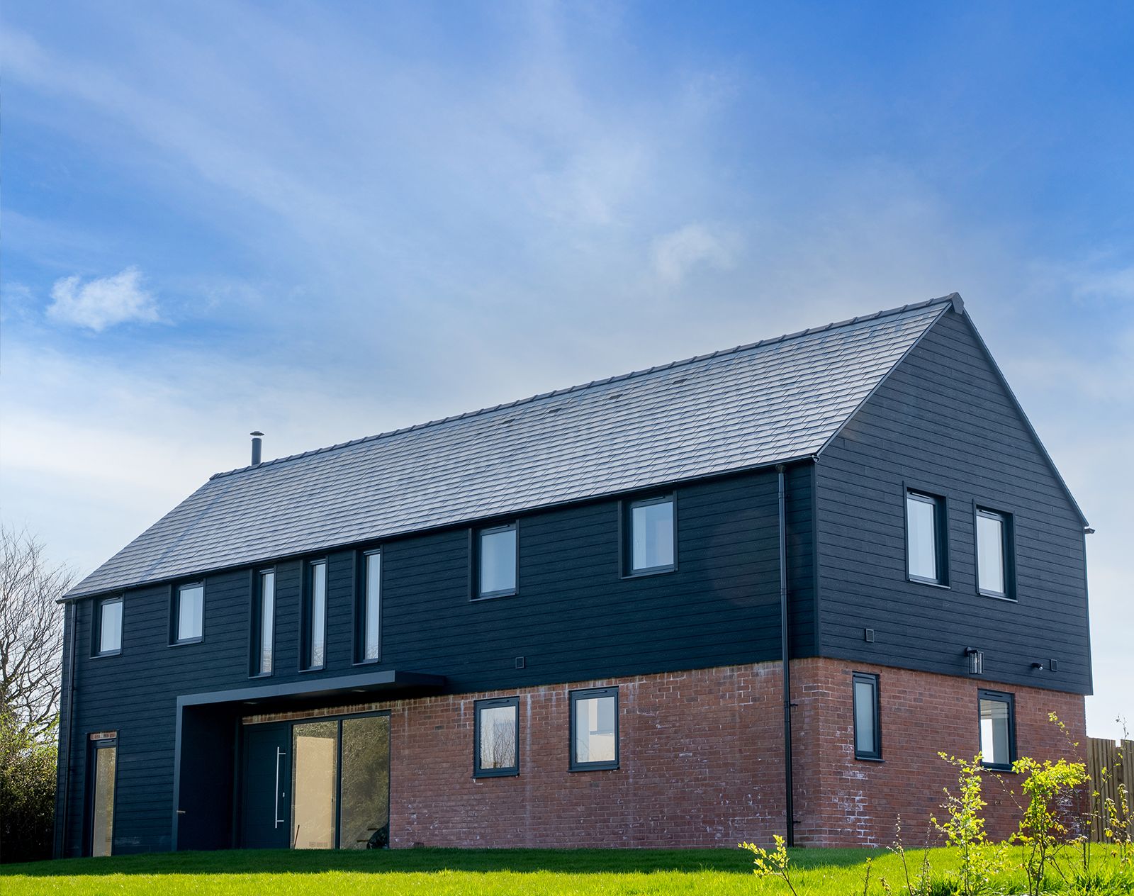 Contemporary home with black horizontal composite cladding on the upper floor and red brickwork on the lower level, combining modern style with durable, low-maintenance materials.