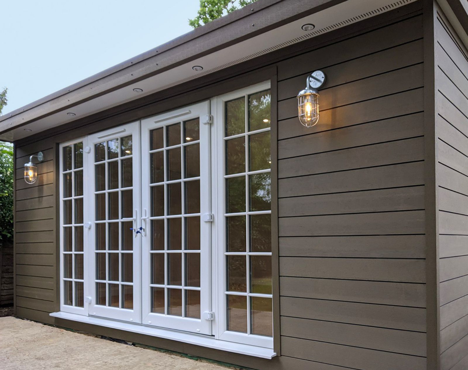 Garden room finished with brown horizontal composite cladding and white French doors, featuring exterior wall lights and a clean modern design.