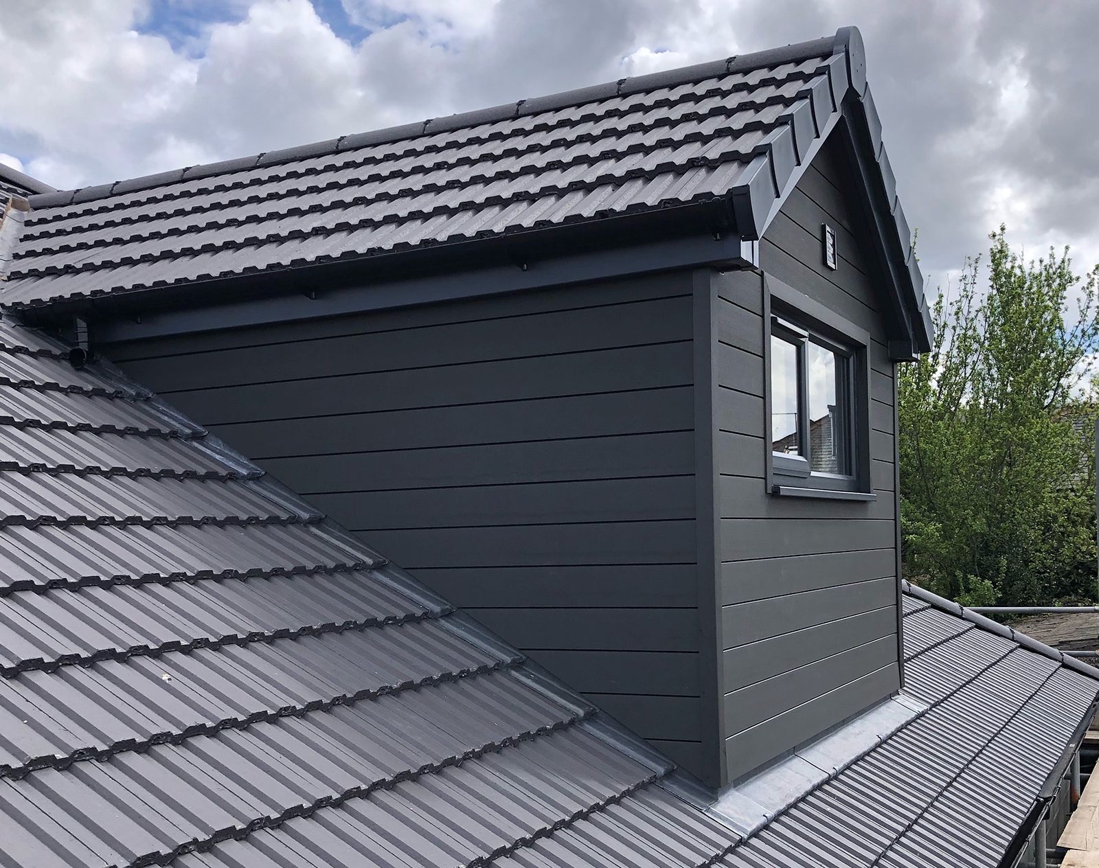 Grey composite cladding used on a modern dormer extension with matching window trim and tiled pitched roof, creating a sleek, weather-resistant finish.