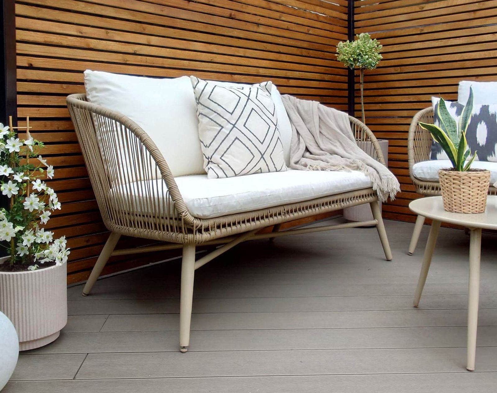 Stylish outdoor seating area with light brown composite decking, rattan garden furniture, and slatted timber privacy screen.
