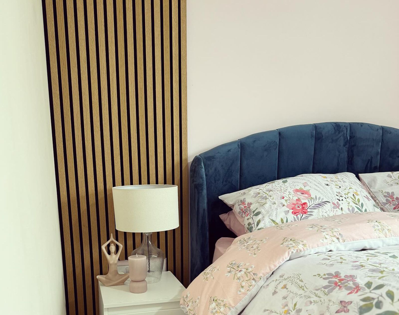 Light oak slatted wall panelling adding a contemporary accent to a bedroom with a velvet blue headboard and floral bedding.