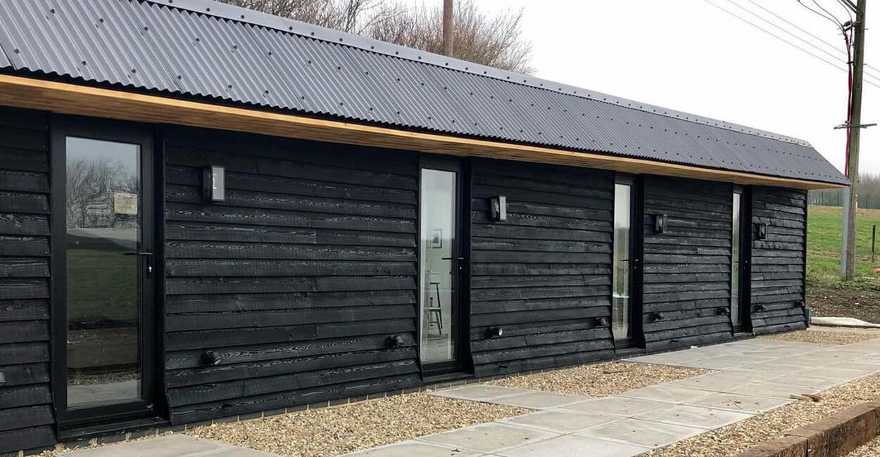 Central courtyard at The Hopper Huts surrounded by restored lodges with Cladco black corrugated steel roofing, offering a communal outdoor space for guests
