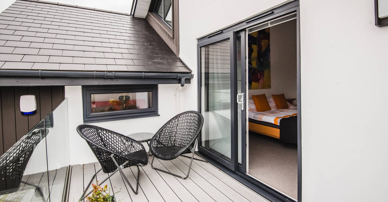 Front exterior of modern timber frame retirement home in Penarth featuring grey composite decking and large sliding doors.