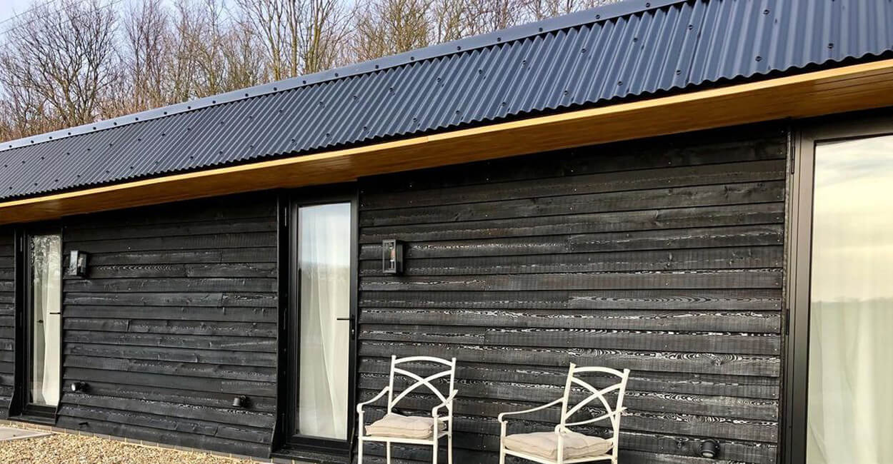 Detail of Cladco 13/3 black PVC Plastisol corrugated steel roofing sheets installed on Hopper Huts, showcasing traditional design with modern materials