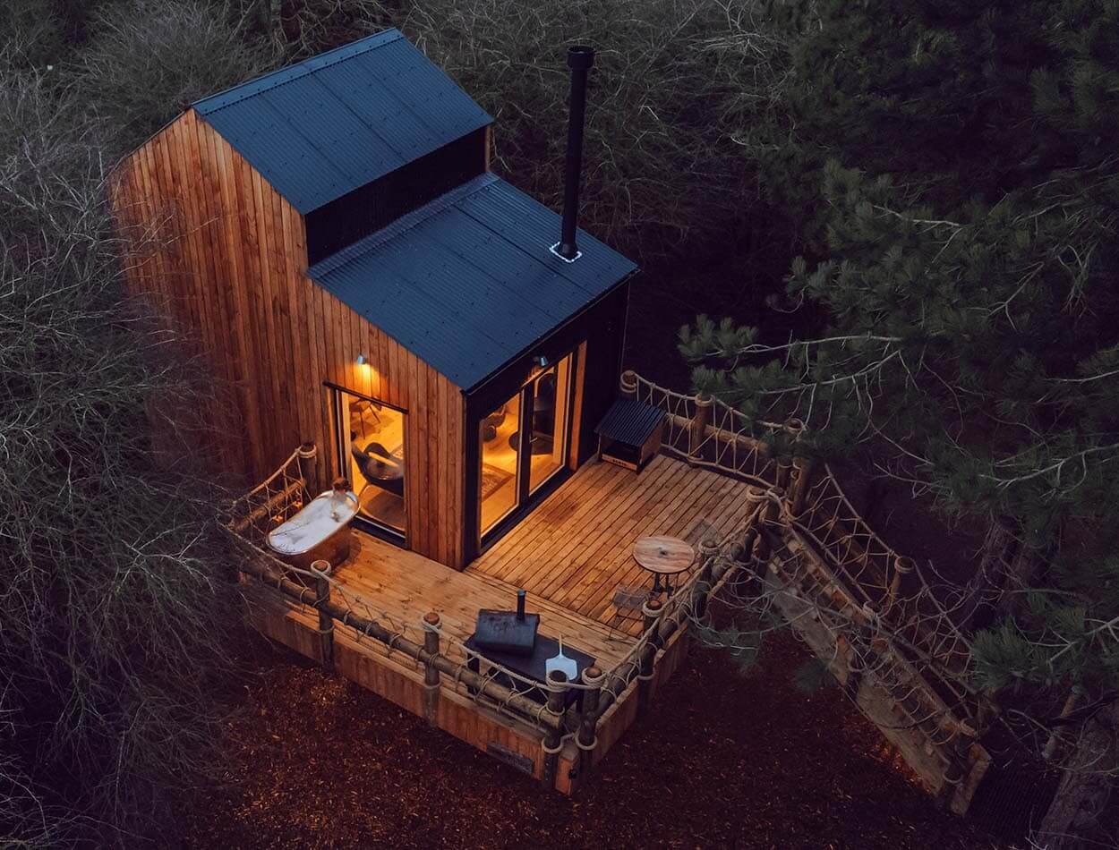 Luxury outdoor copper bath and wood burner on deck of Two Pines treehouse at The Wilding Airfield
