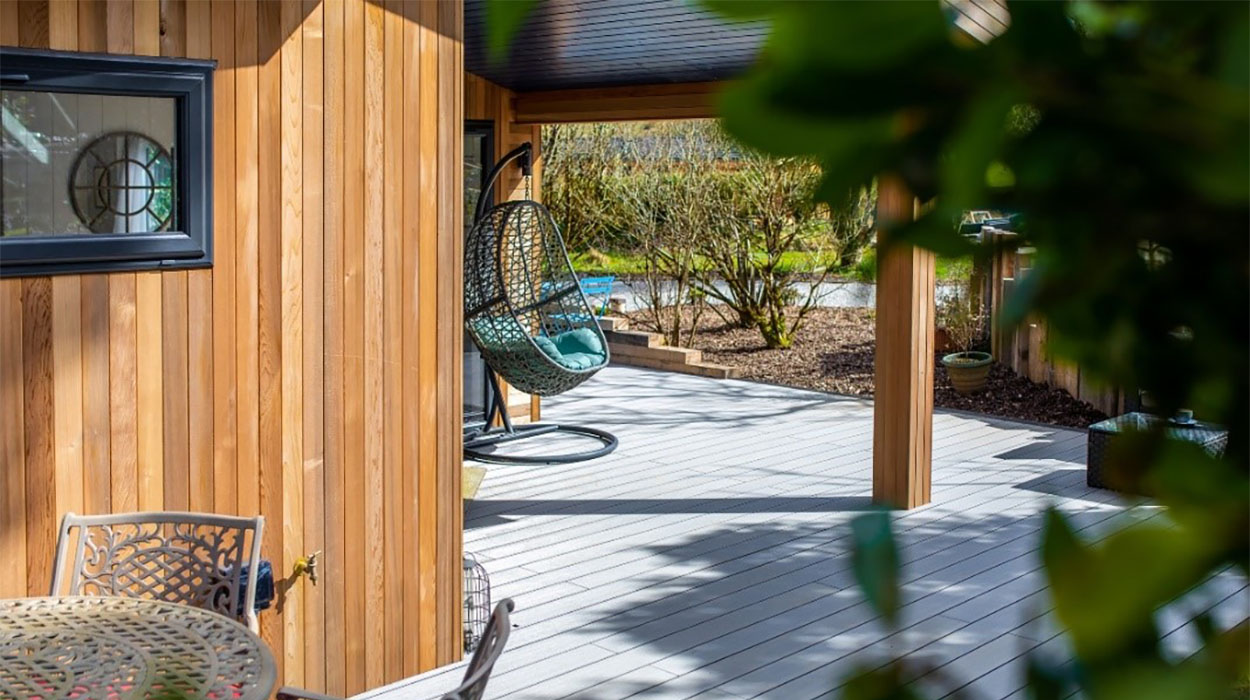 Stone Grey Cladco Composite Decking with outdoor furniture beside timber holiday home in rural setting