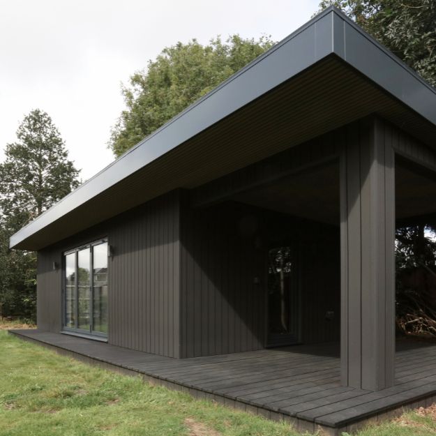 Garden art studio with bifold doors, clad in Cladco Charcoal Composite Cladding and Decking, seamlessly blending with woodland surroundings
